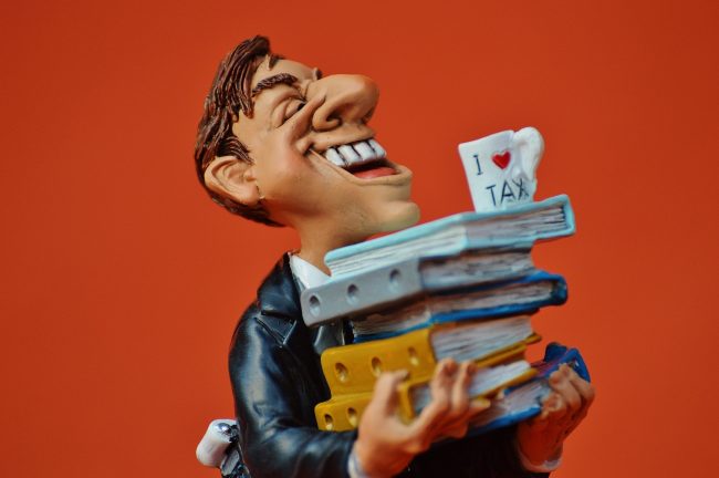 tax-consultant Cartoonish picture of a man balancing an I love Tax mug on top of a pile of files.